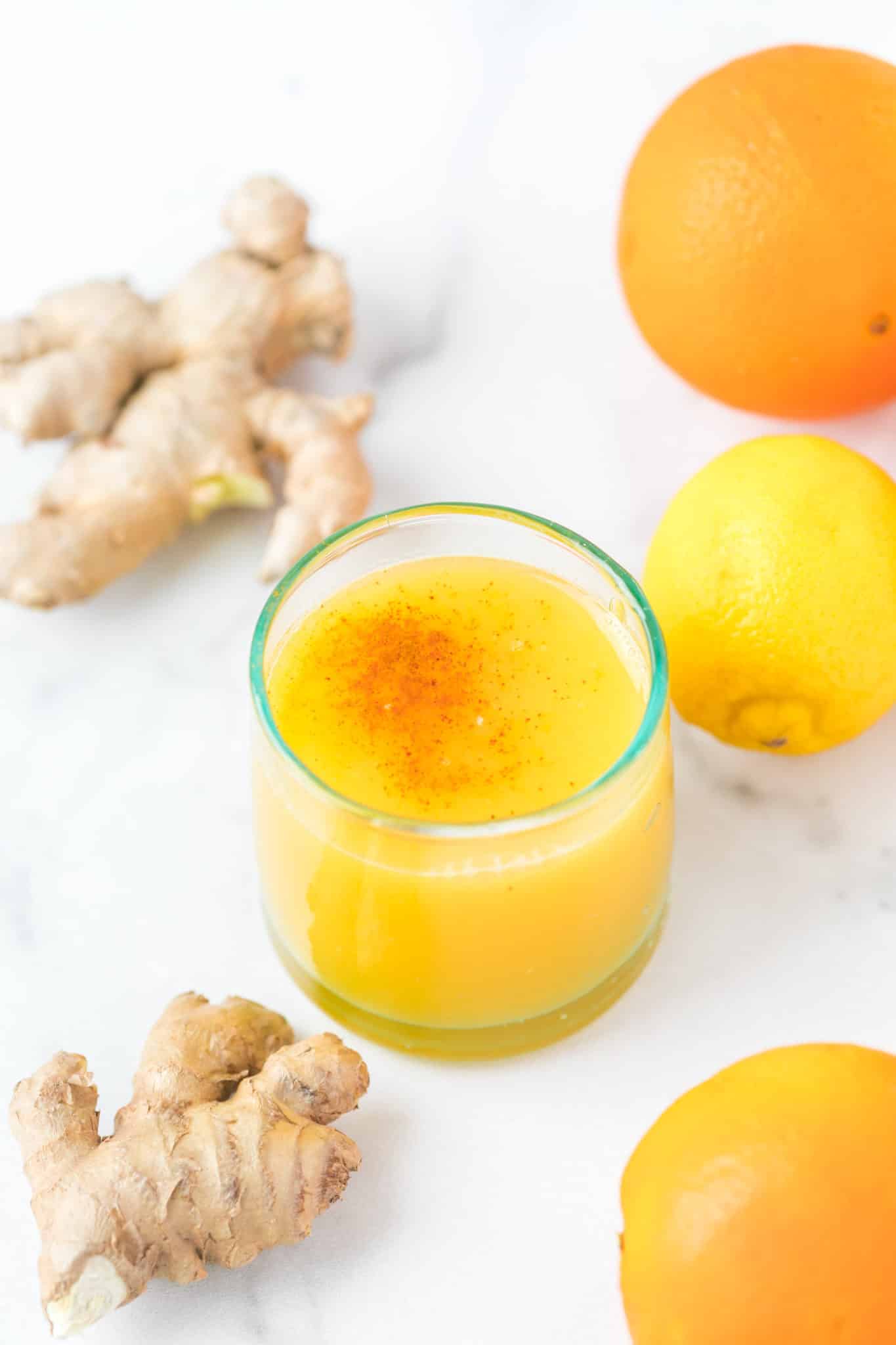 glass of lemon ginger shot on table with fresh ginger root.