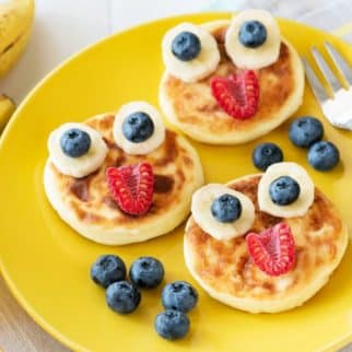 Pancakes with fruit faces on a yellow plate.