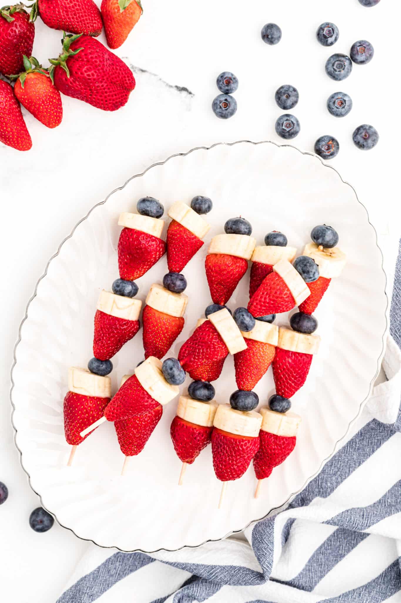 Red white and blue patriotic fruit kabobs on a white platter.