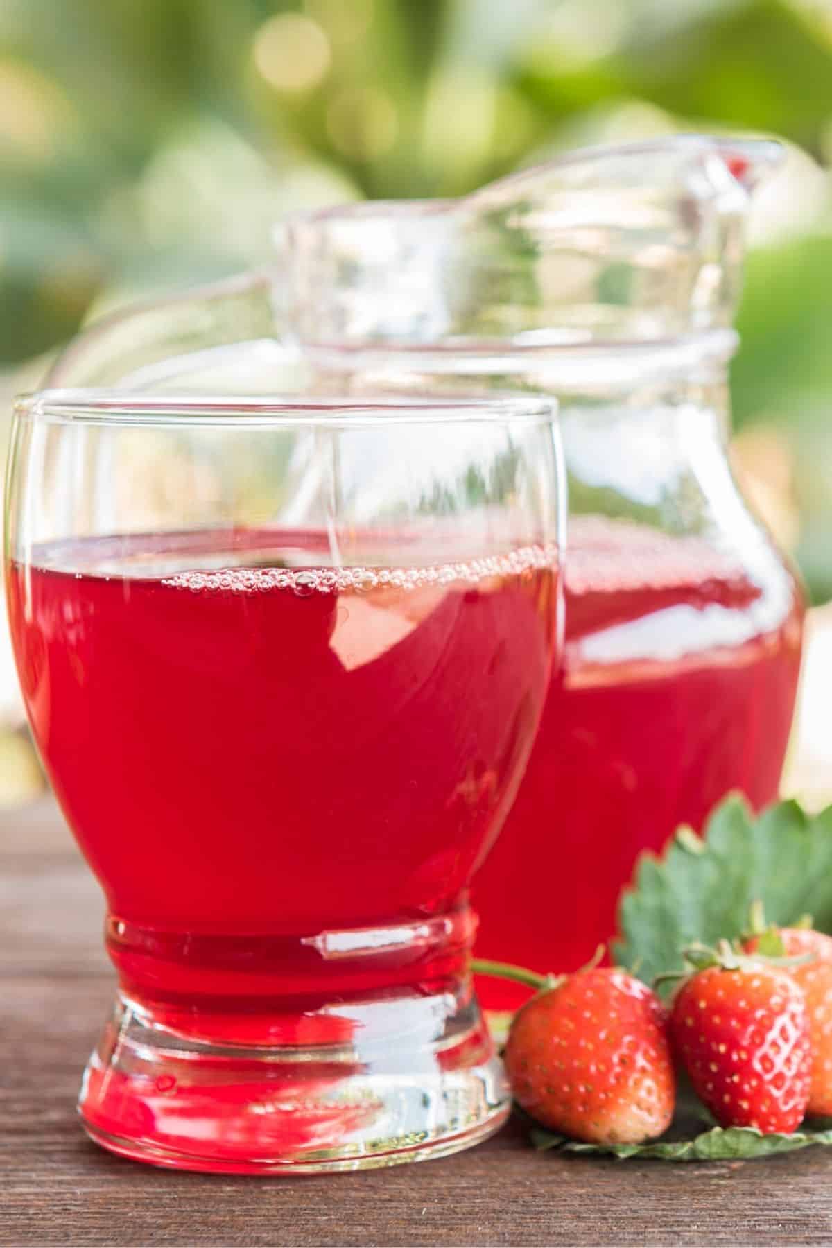 pitcher and glass of strawberry juice on a table outside.