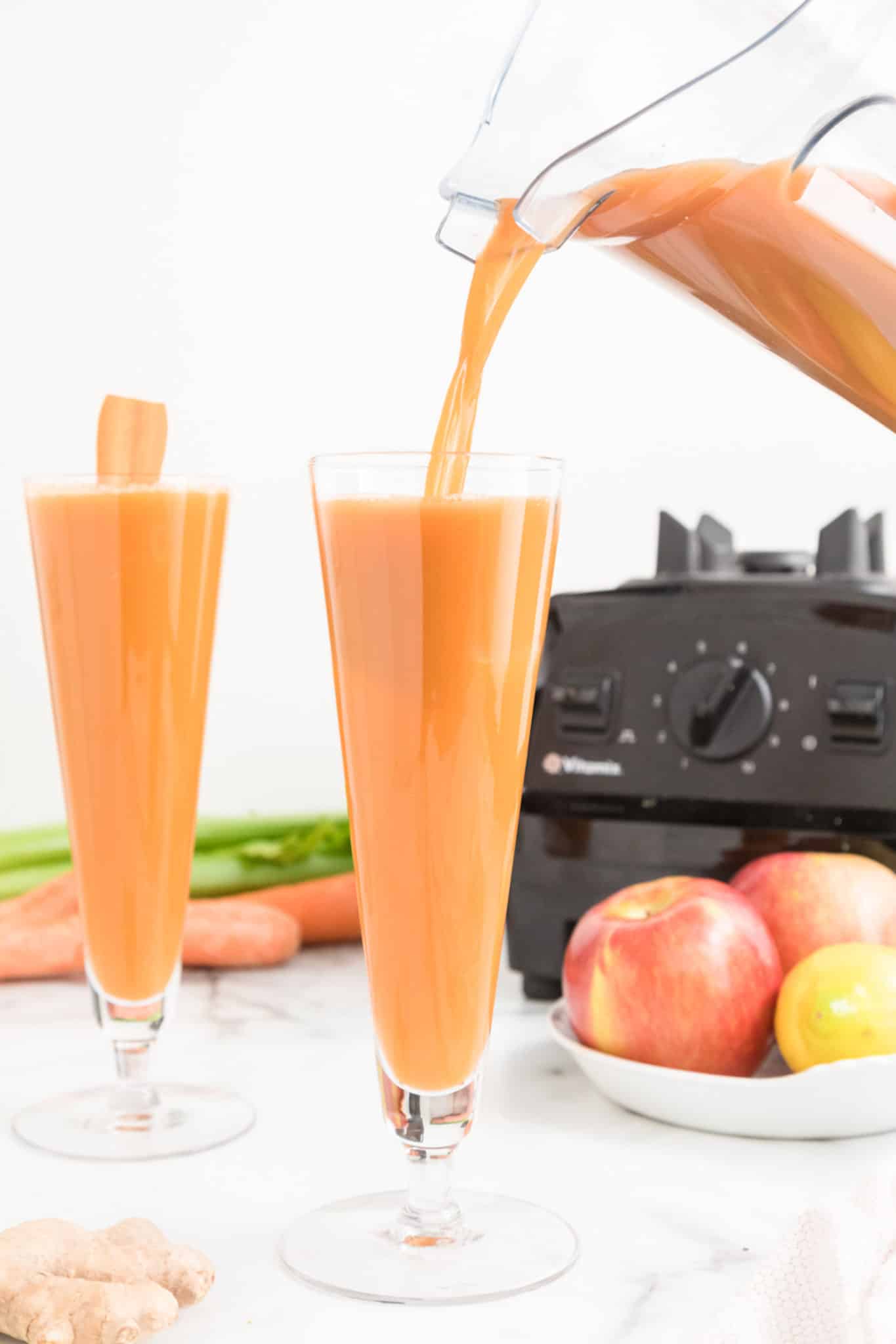 A blender pouring carrot celery juice into a glass.