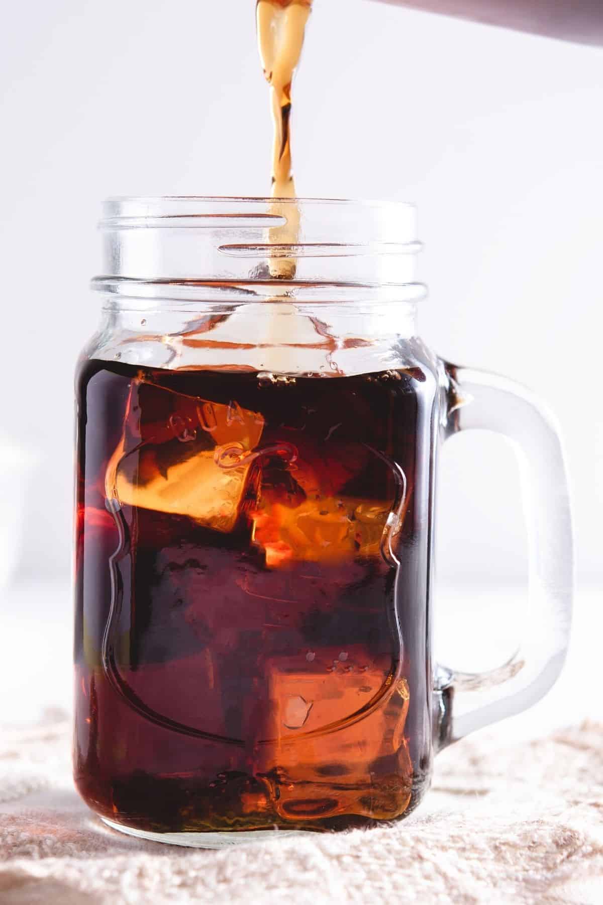 pouring cold brew coffee over ice in a mug.