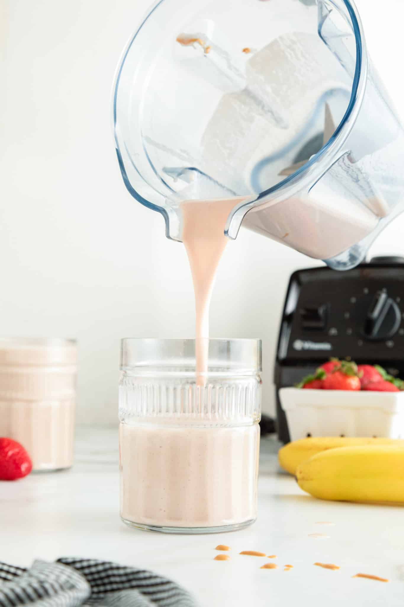 A blender jar pouring a strawberry banana PB smoothie into a glass.