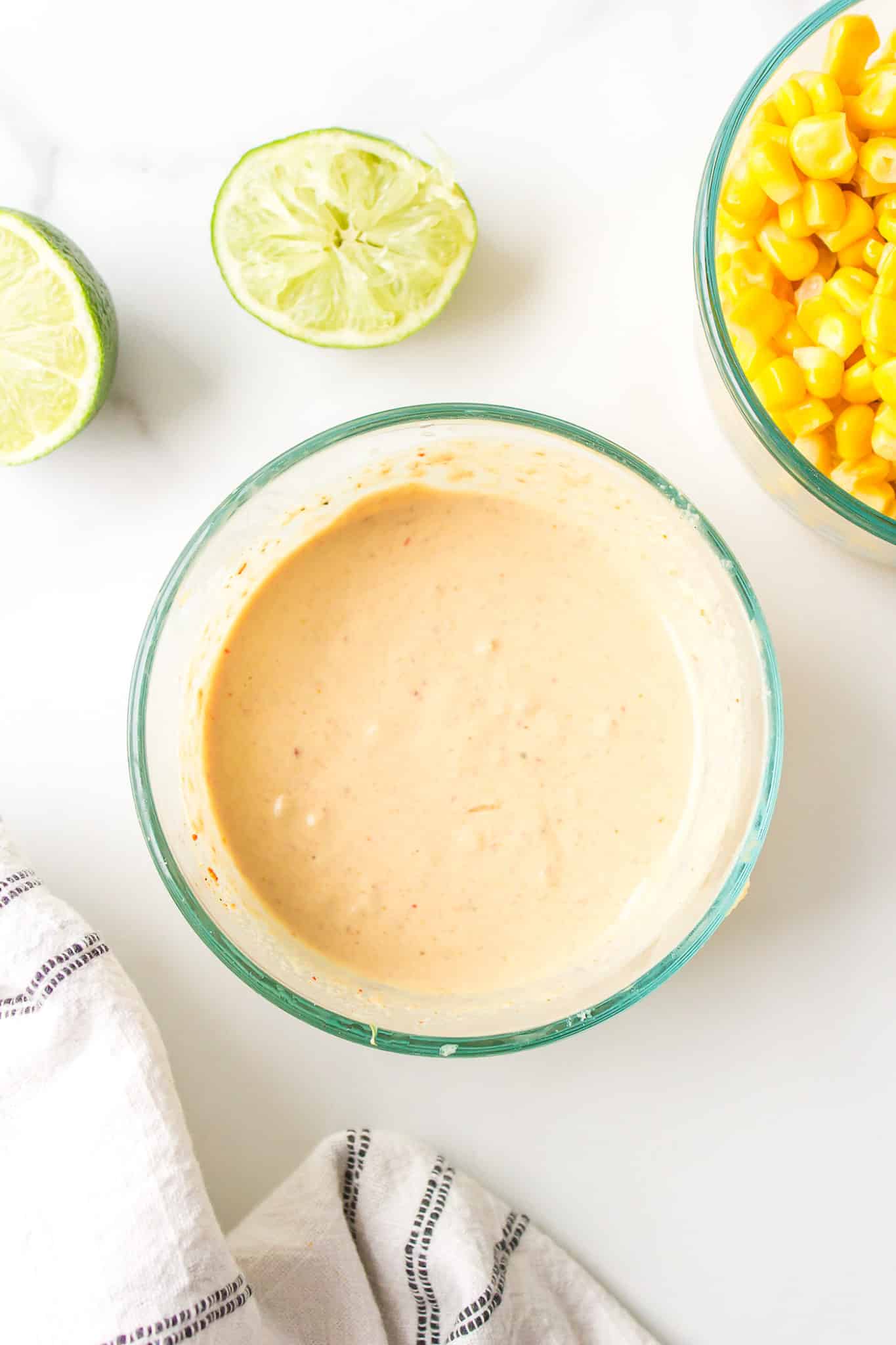 Spicy tahini sauce in a small glass bowl next to a bowl of corn.