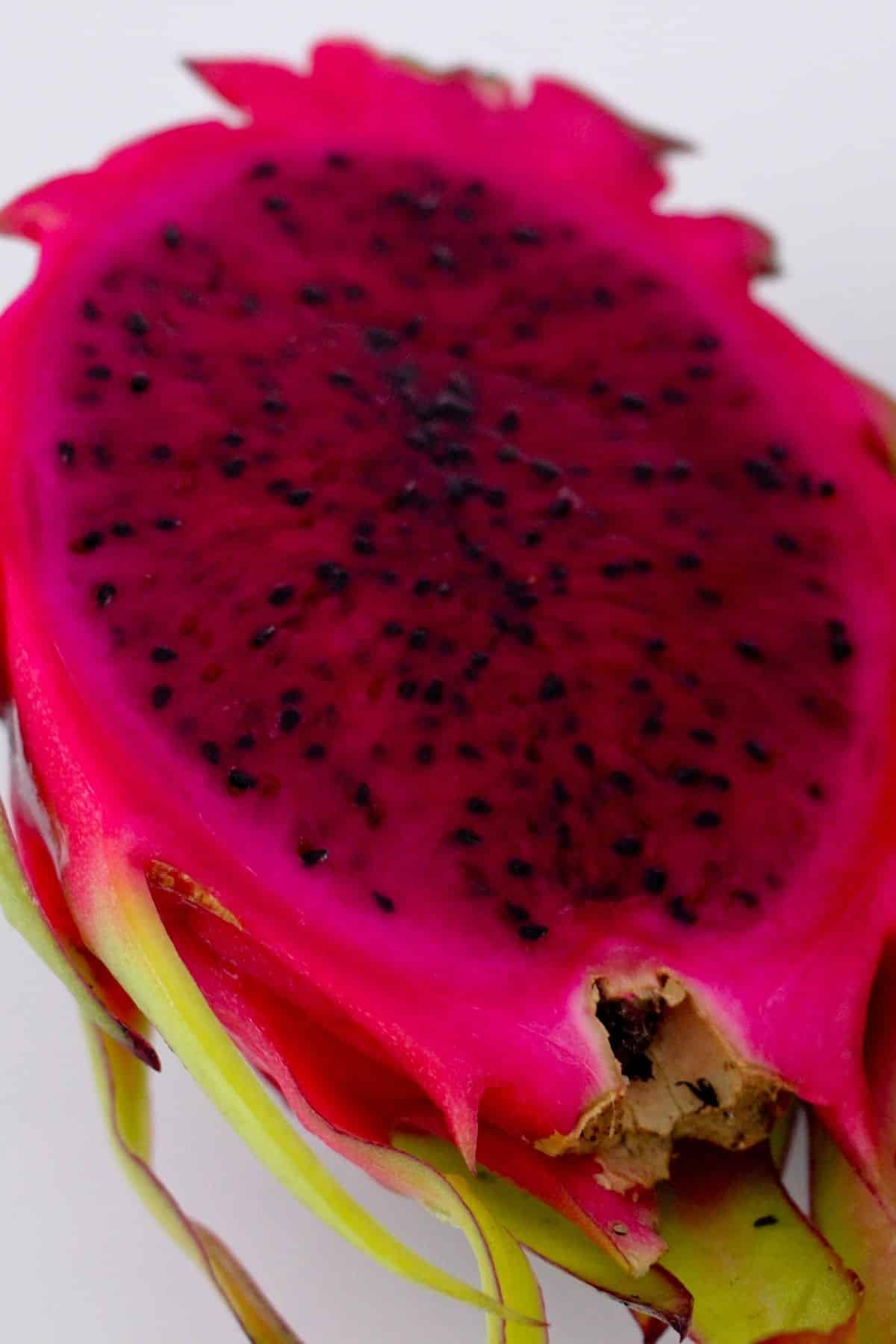 Red flesh dragonfruit cut in half on a white surface.
