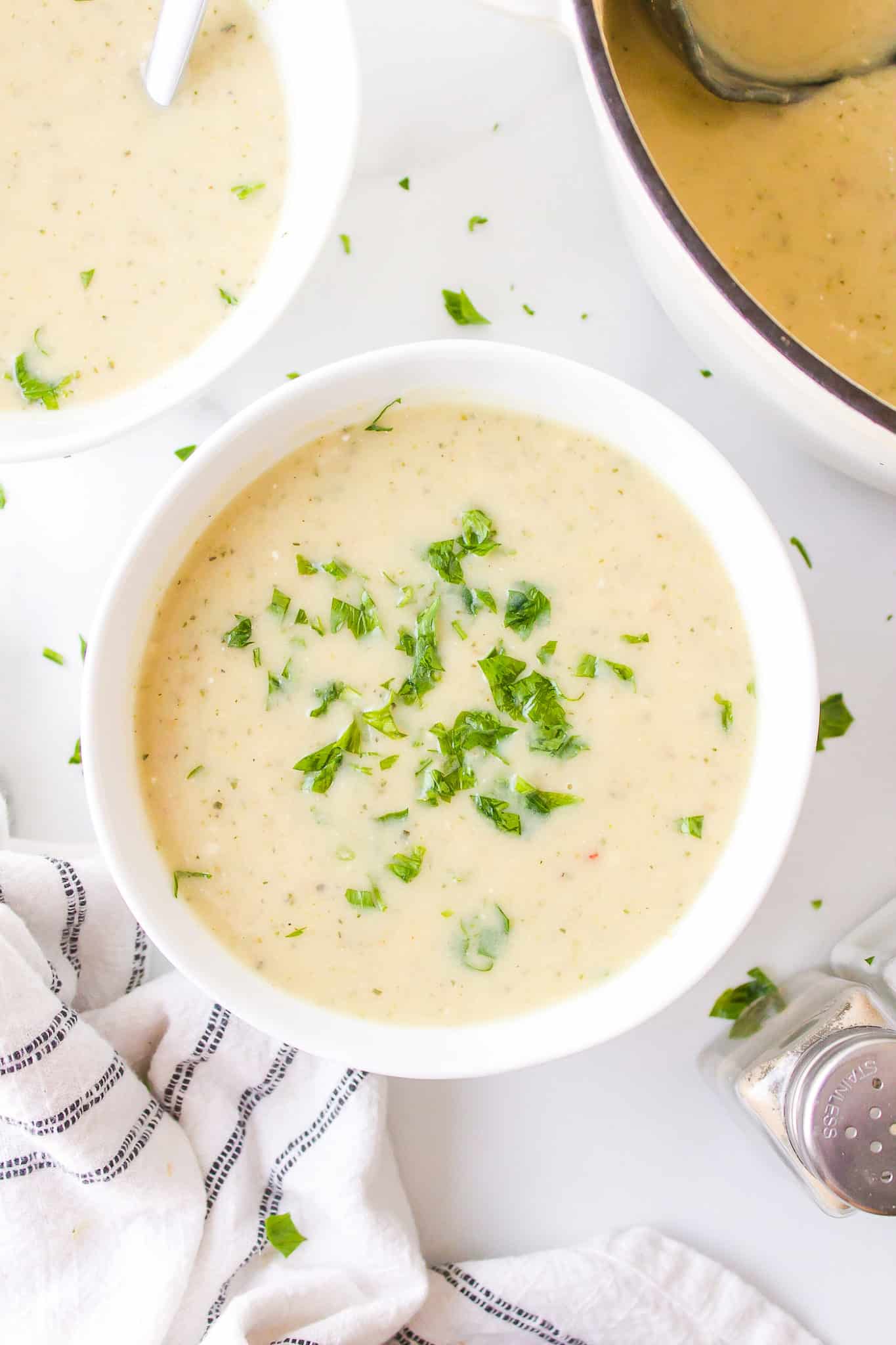 A small white bowl of zucchini potato soup garnished with parsley.