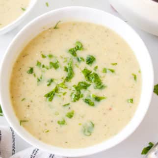 A small white bowl of zucchini potato soup garnished with parsley.