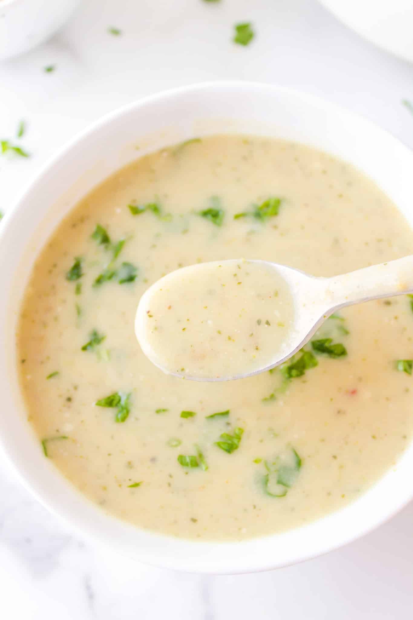 A silver spoon lifting a bite of potato soup from a white bowl.
