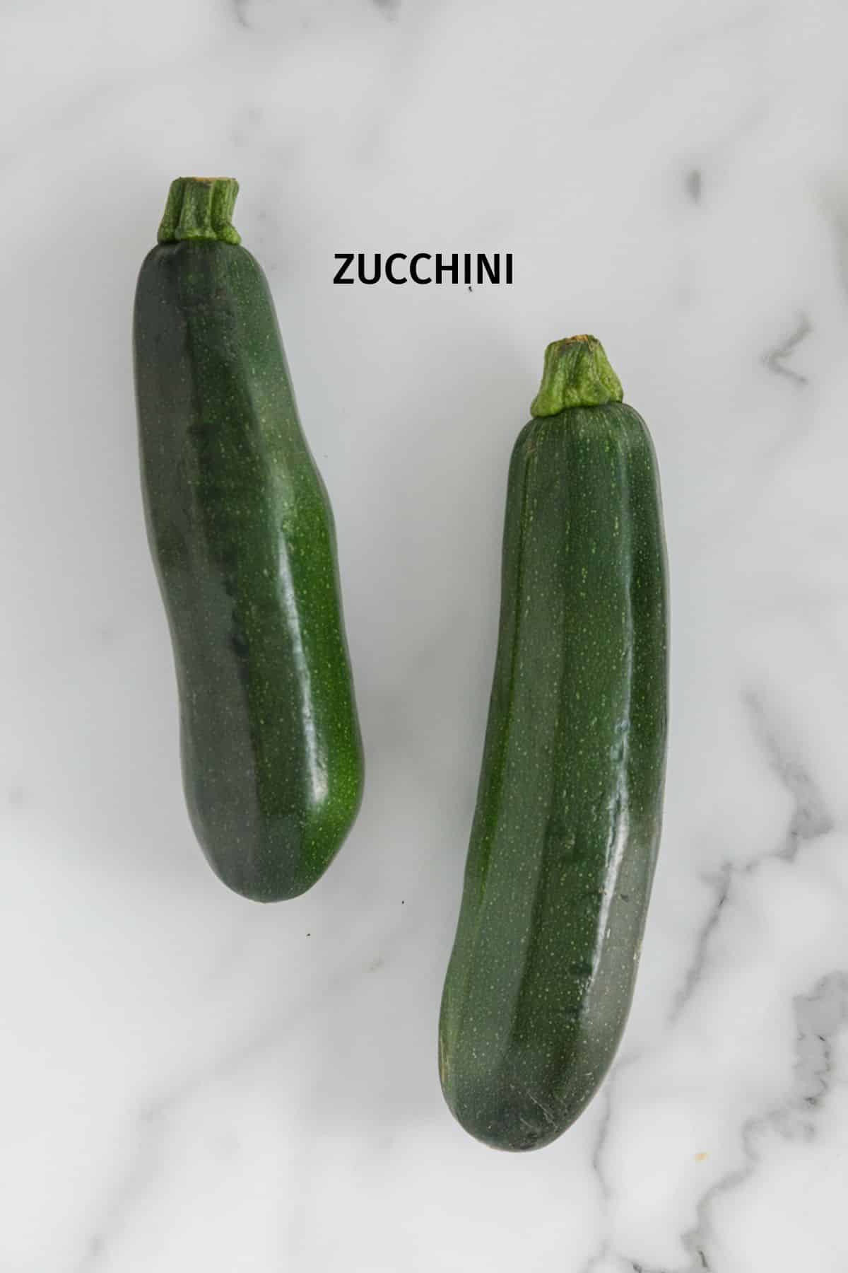 Two whole zucchini on a white marble surface.