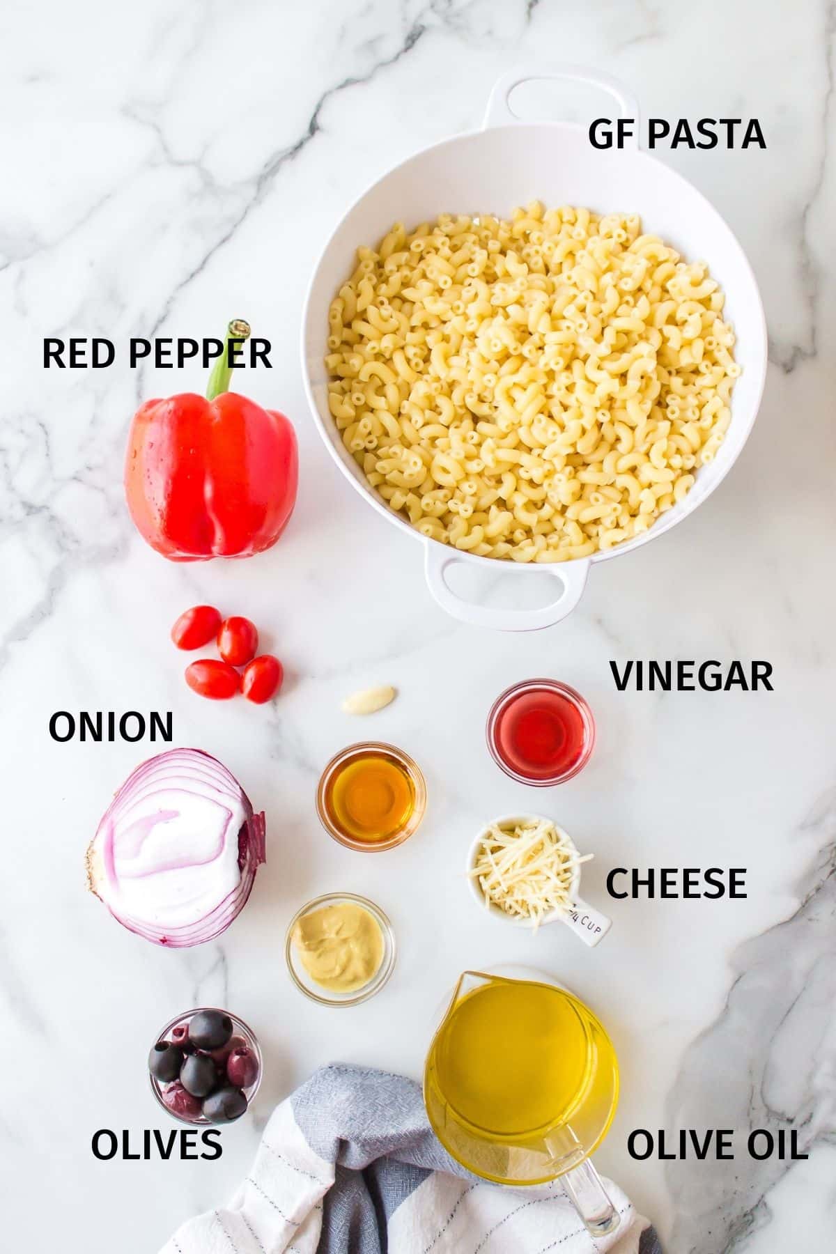 Ingredients for pasta salad in small bowls on a white surface.