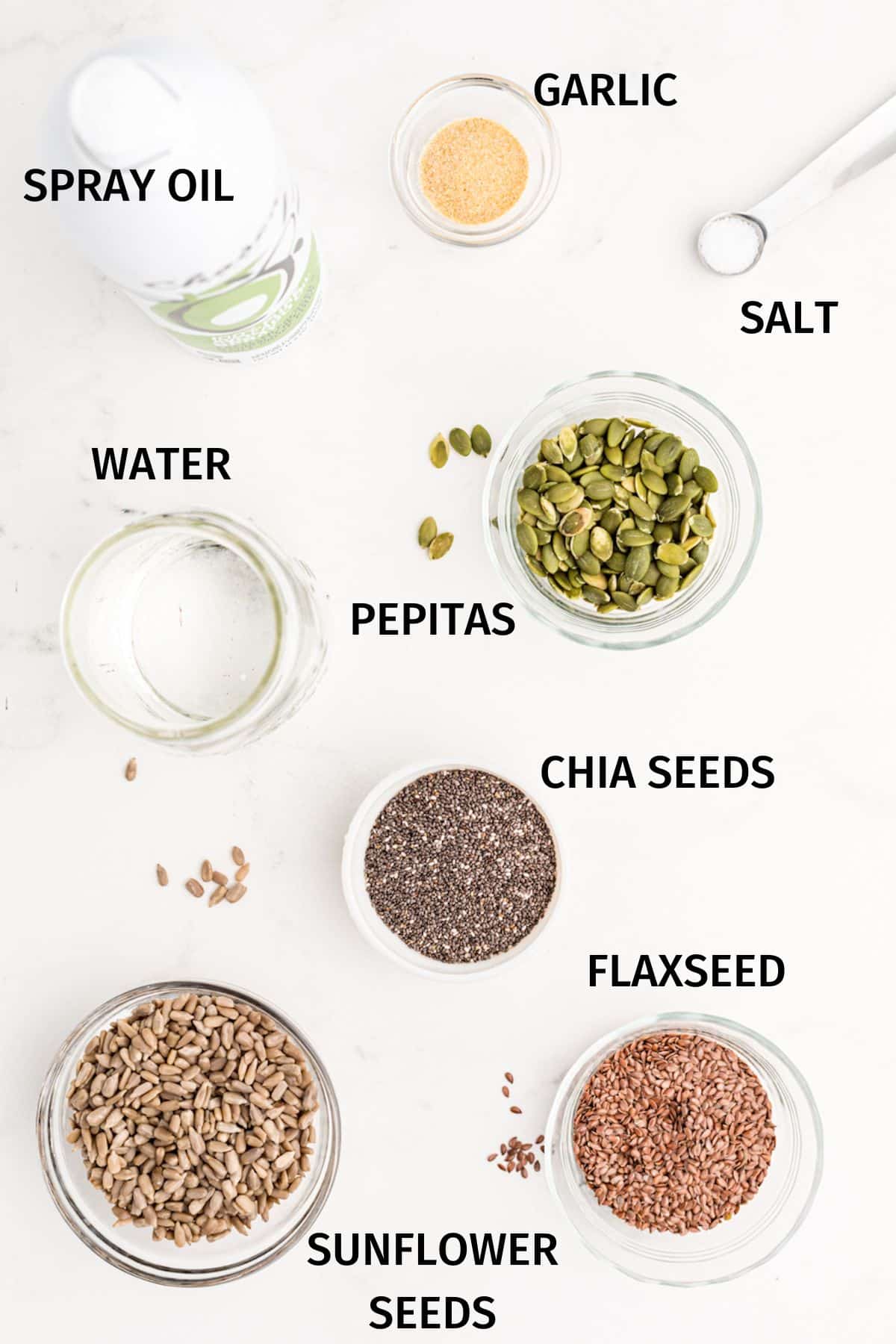 Ingredients to make seed crackers in small bowls on a white surface.
