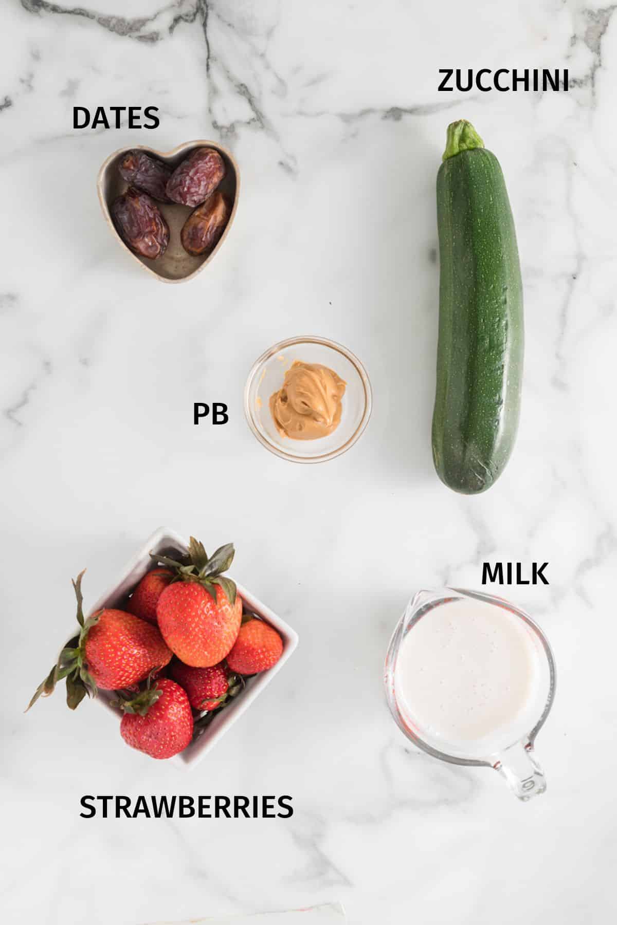 Ingredients for a strawberry zucchini smoothie on a white marble surface.