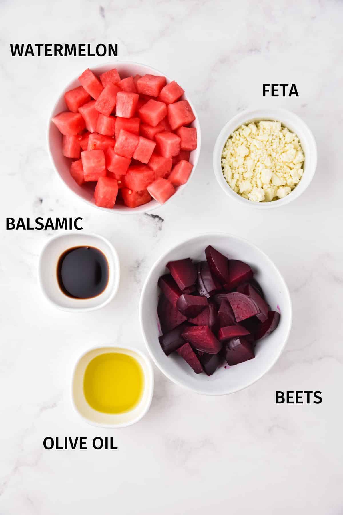 Ingredients for watermelon beet salad in small white bowls on a white surface.
