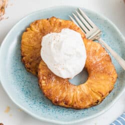 Two air fried pineapple rings topped with whipped cream on a small blue plate.