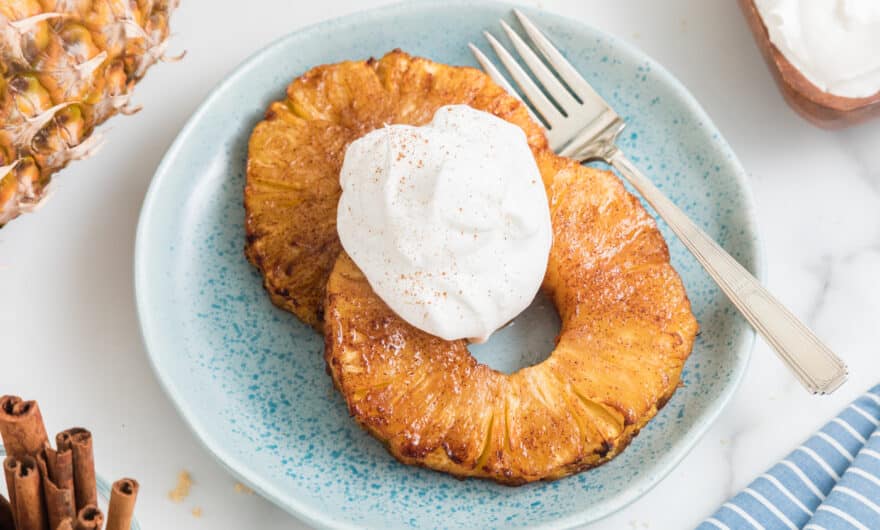 Two air fried pineapple rings topped with whipped cream on a small blue plate.