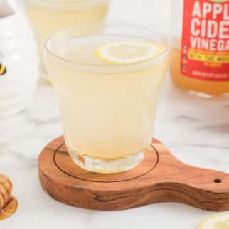 A glass of lemon apple cider vinegar water with a floating lemon wheel.