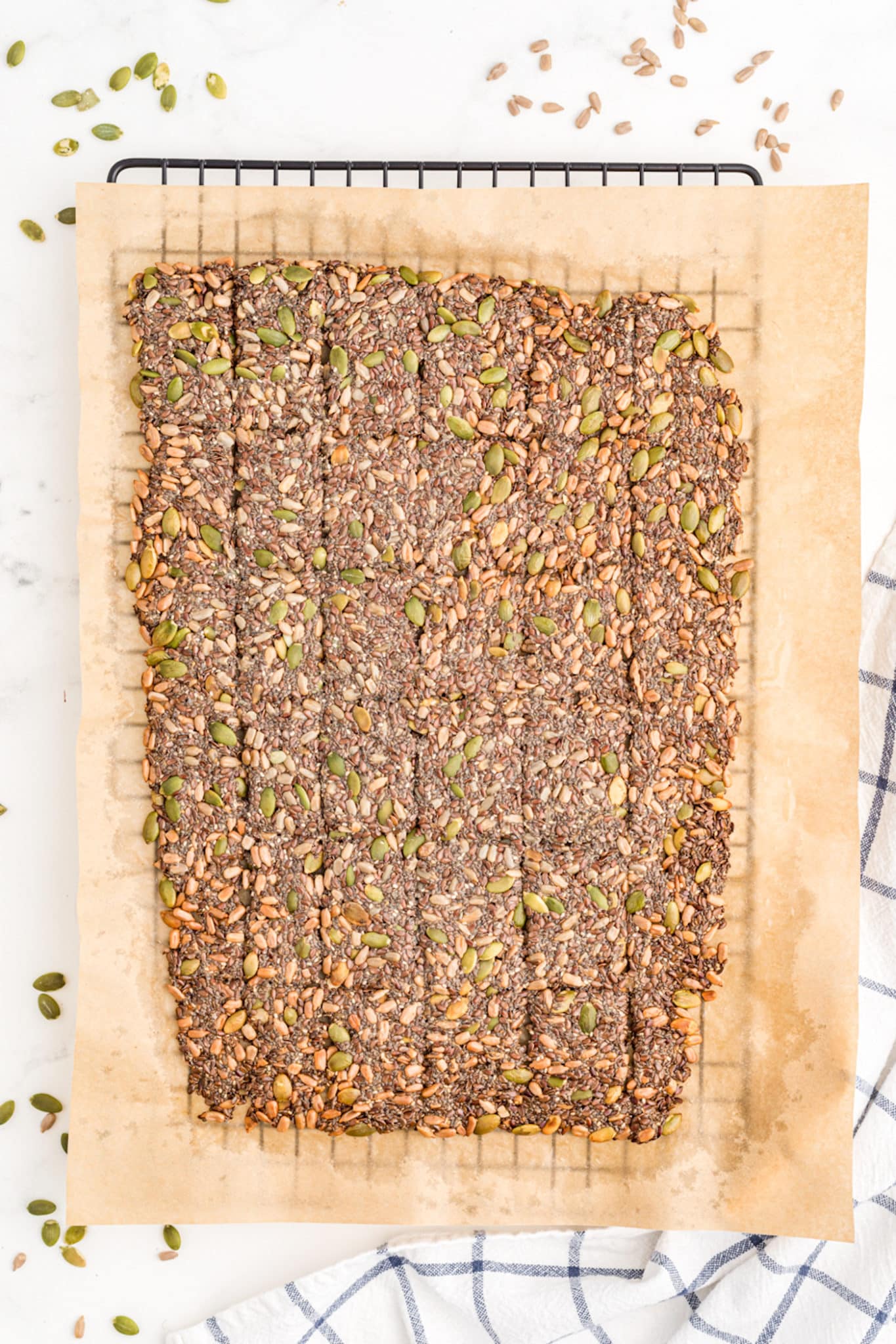 A slab of seed crackers on parchment paper set on a wire cooling rack.