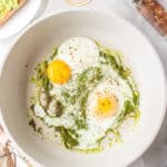 Two eggs in a skillet of warmed pesto.