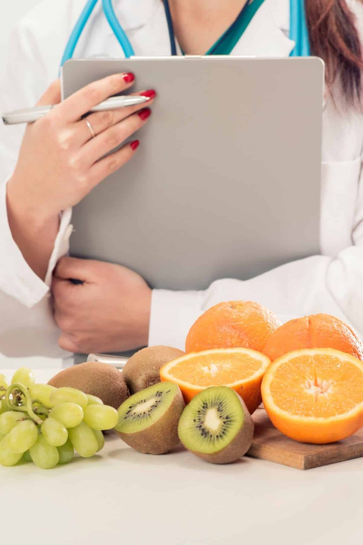 A doctor in white cold holding a clipboard in front of fruit on a table.