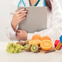 A doctor in white cold holding a clipboard in front of fruit on a table.