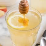 Drizzling honey into a glass of lemon apple cider water.