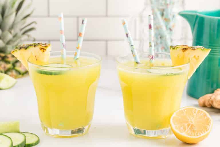 Two glasses of pineapple cucumber juice each with two straws.