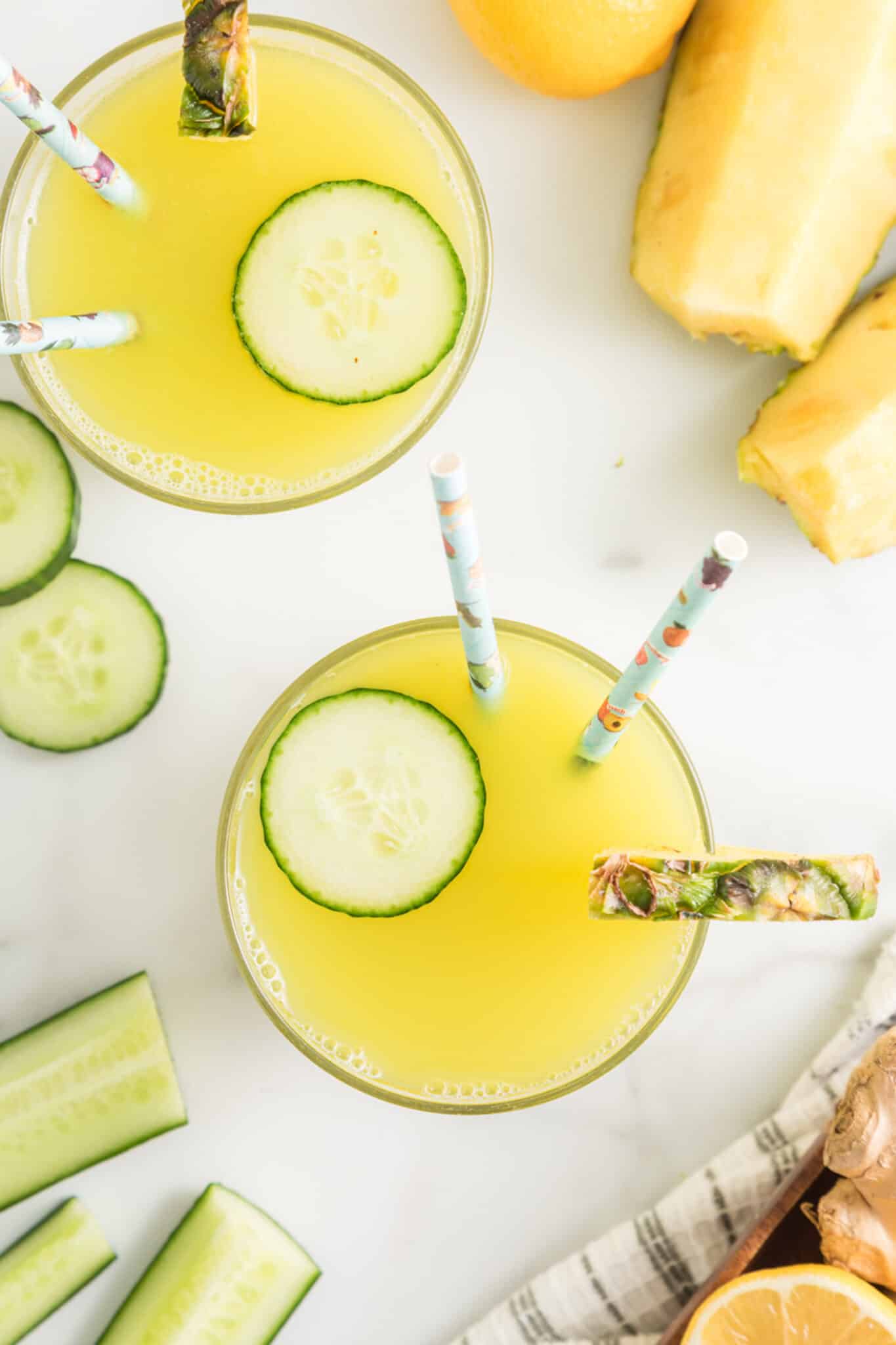 Top view of two glasses of pineapple cucumber juice each with two straws.