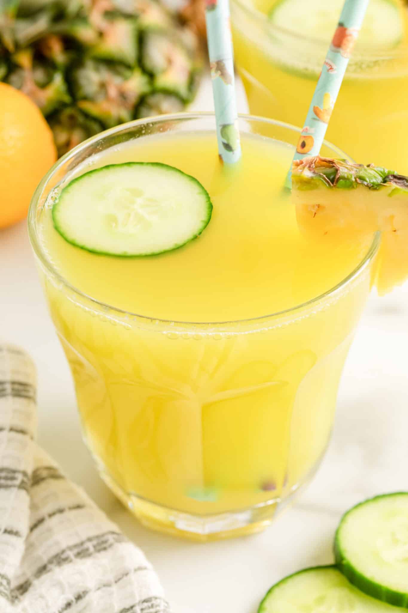 Closeup of a glass of pineapple cucumber juice with two straws.