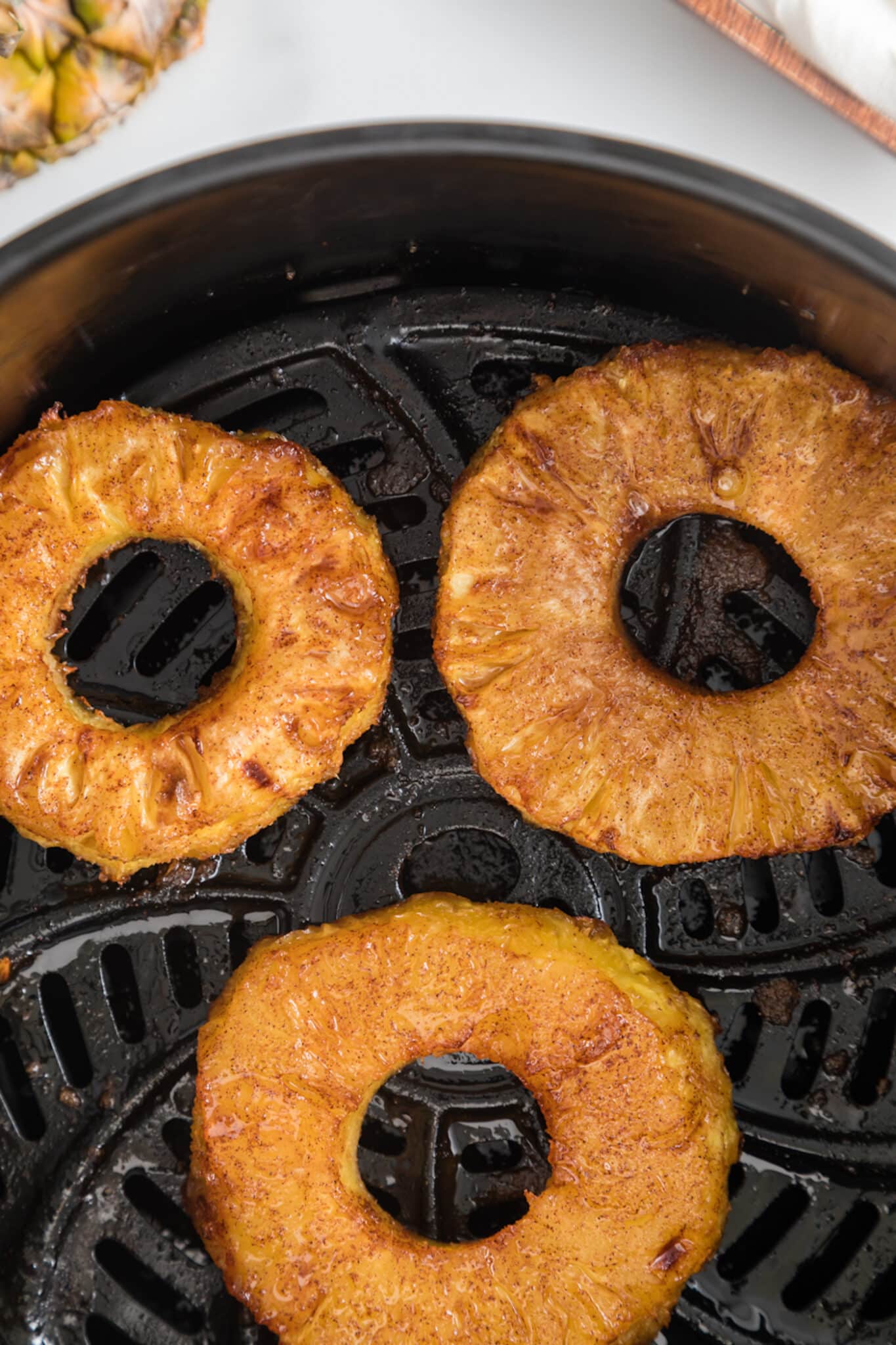 Air fried pineapple rings in the basket of an air fryer.