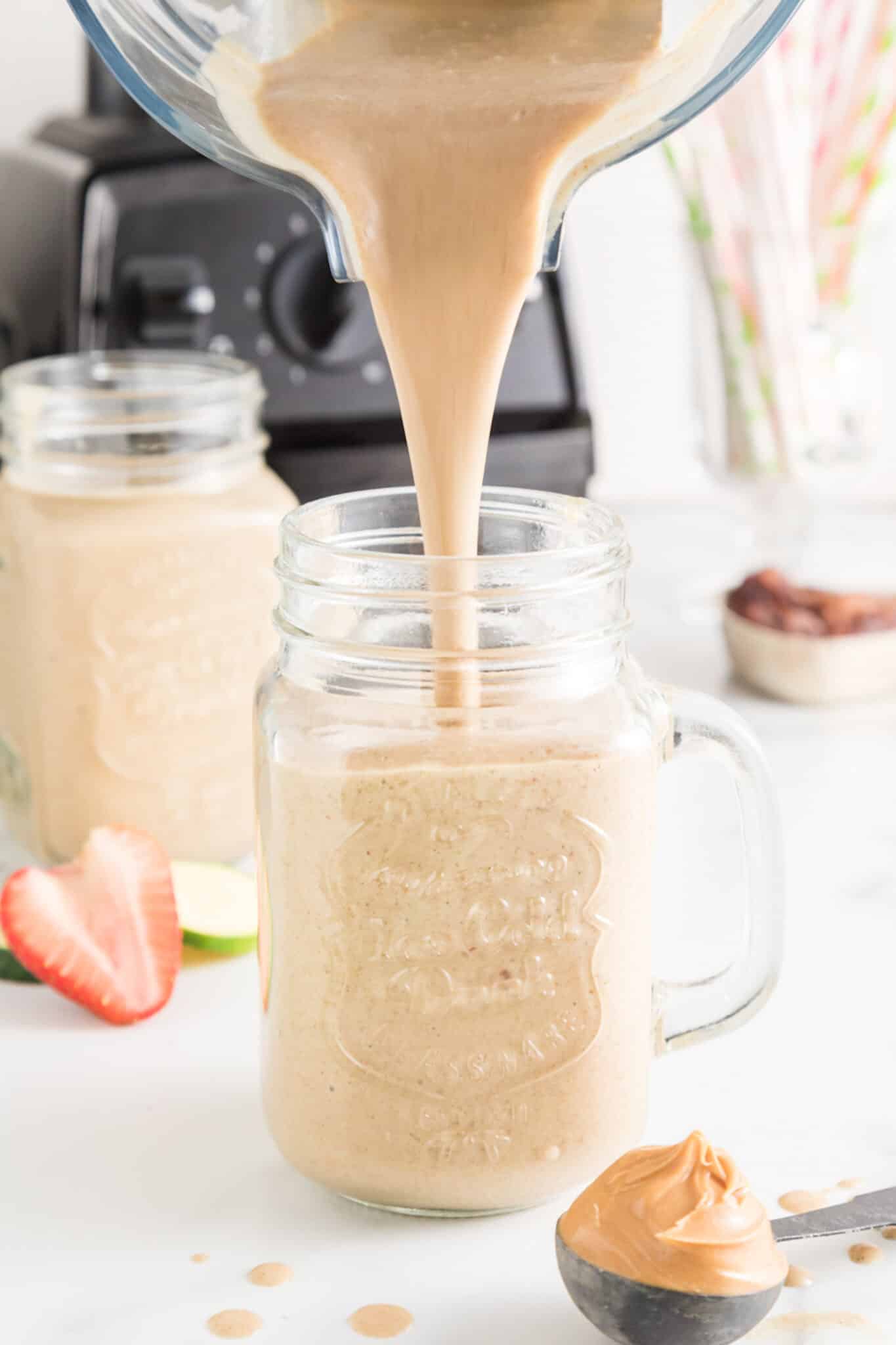A strawberry zucchini smoothie being poured from a blender into a mason jar.