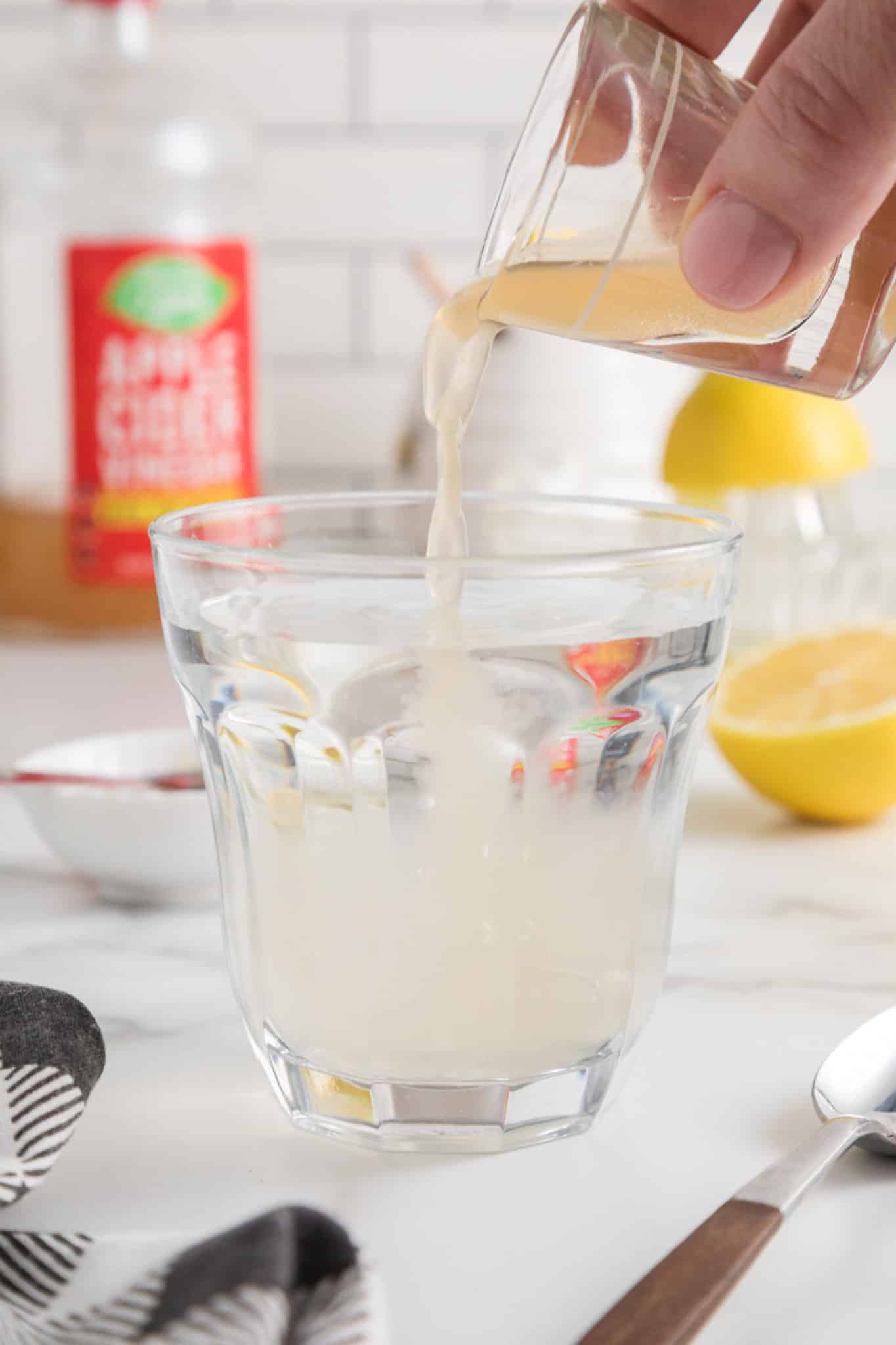 Pouring a shot of apple cider vinegar into a glass of water.