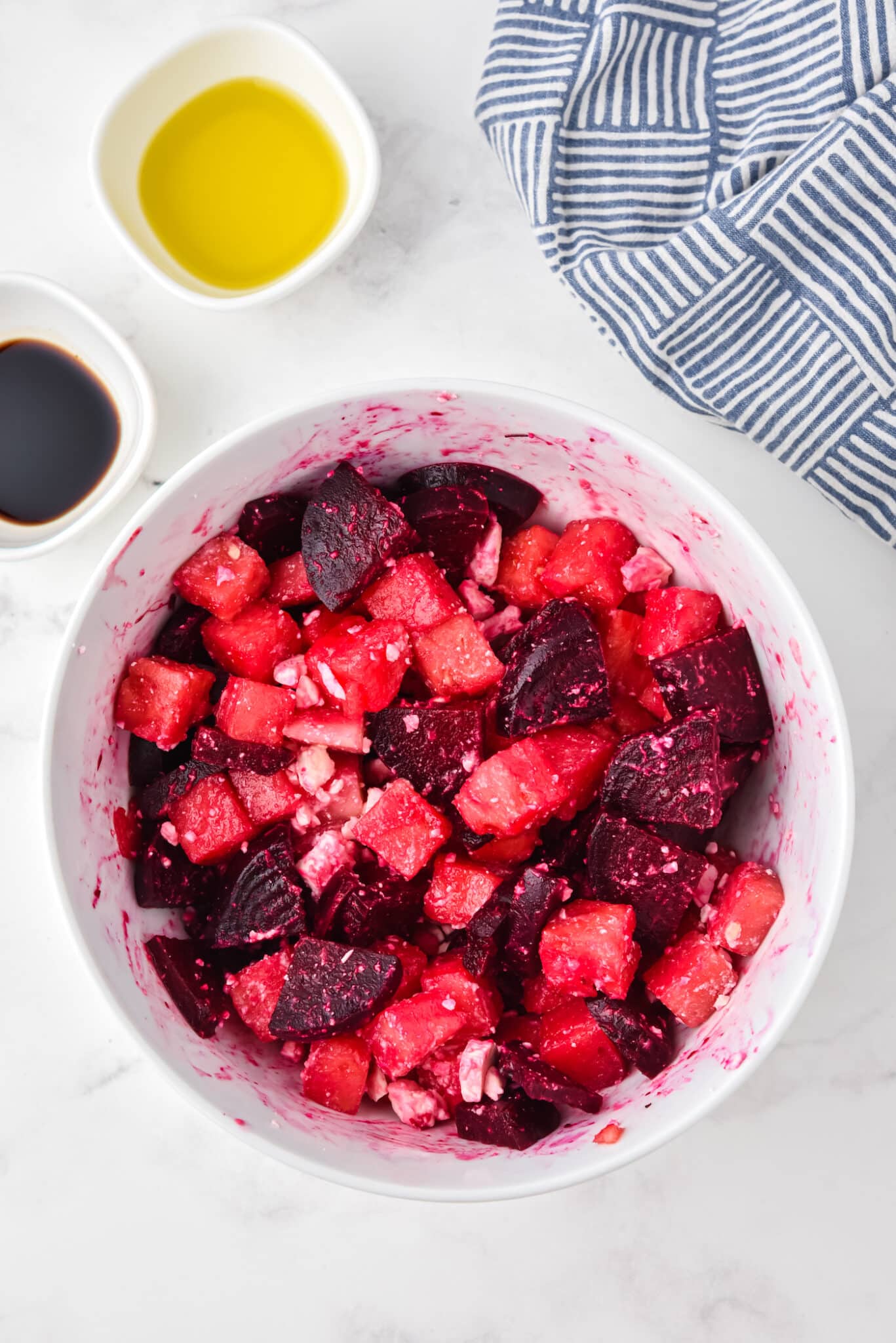 Drizzling and stirring in dressing to a bowl of watermelon beet salad.