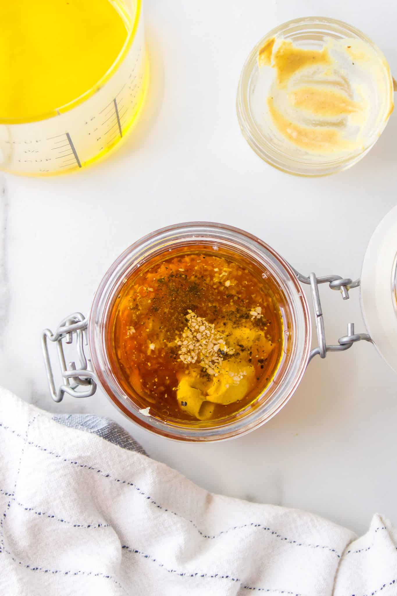 A flip top glass jar filled with dijon mustard dressing ingredients.