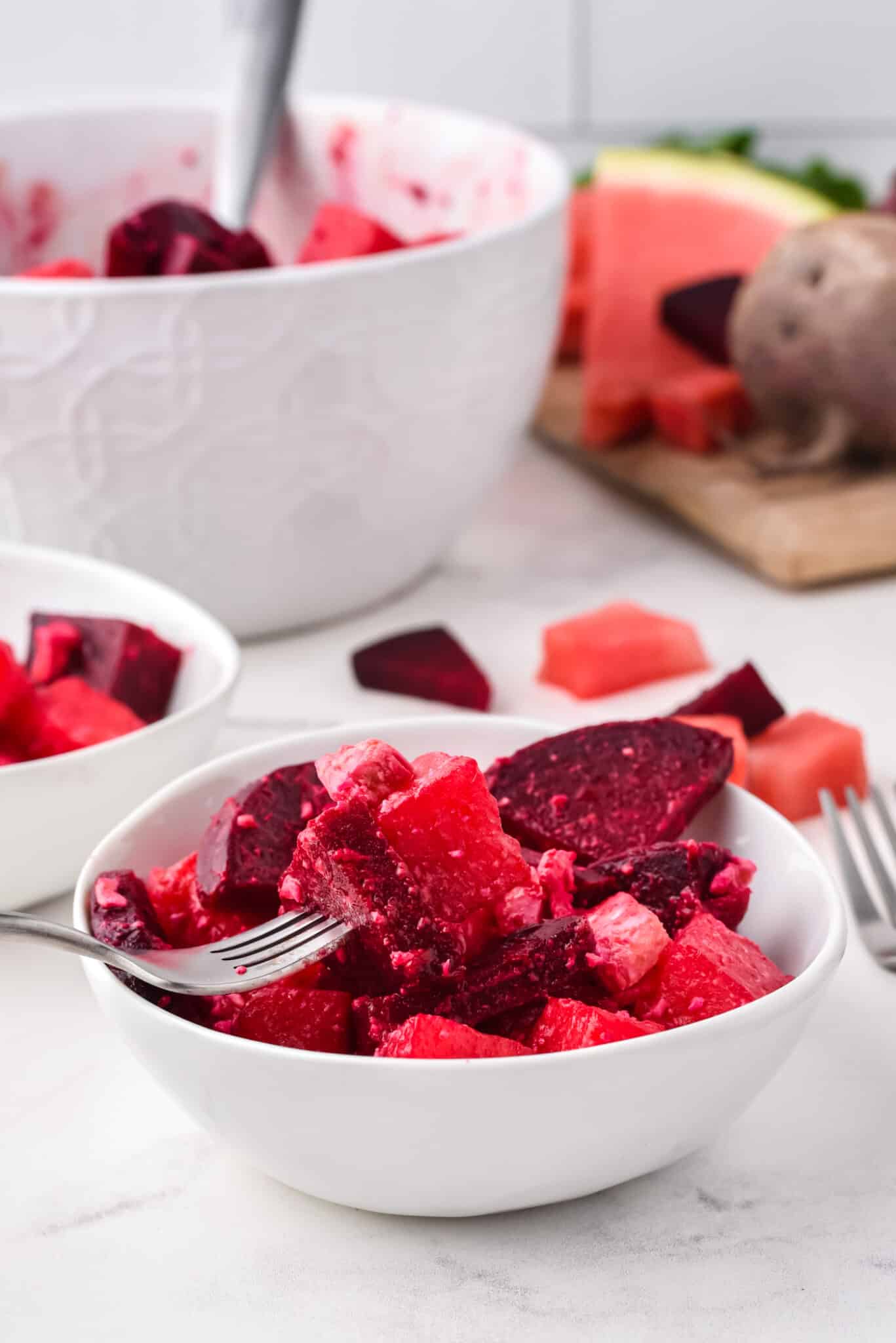 A fork holding a bite of watermelon beet salad over a small white bowl.