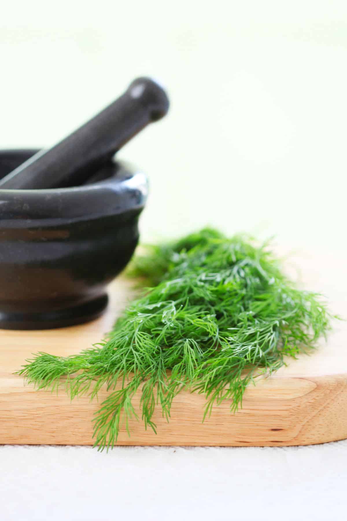 Cutting board with fresh dill and mortar and pestle.