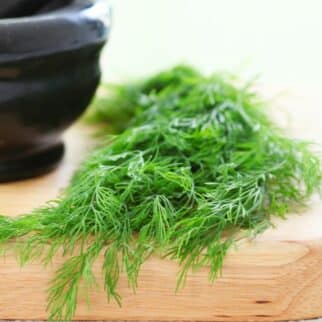 Fresh dill on cutting board with mortar and pestle.