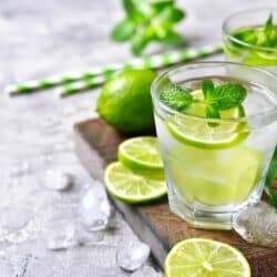 Clear glass filled with mint mojito mocktail on a table with limes and mint.