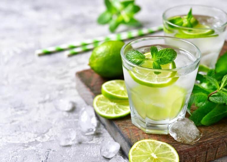 Clear glass filled with mint mojito mocktail on a table with limes and mint.