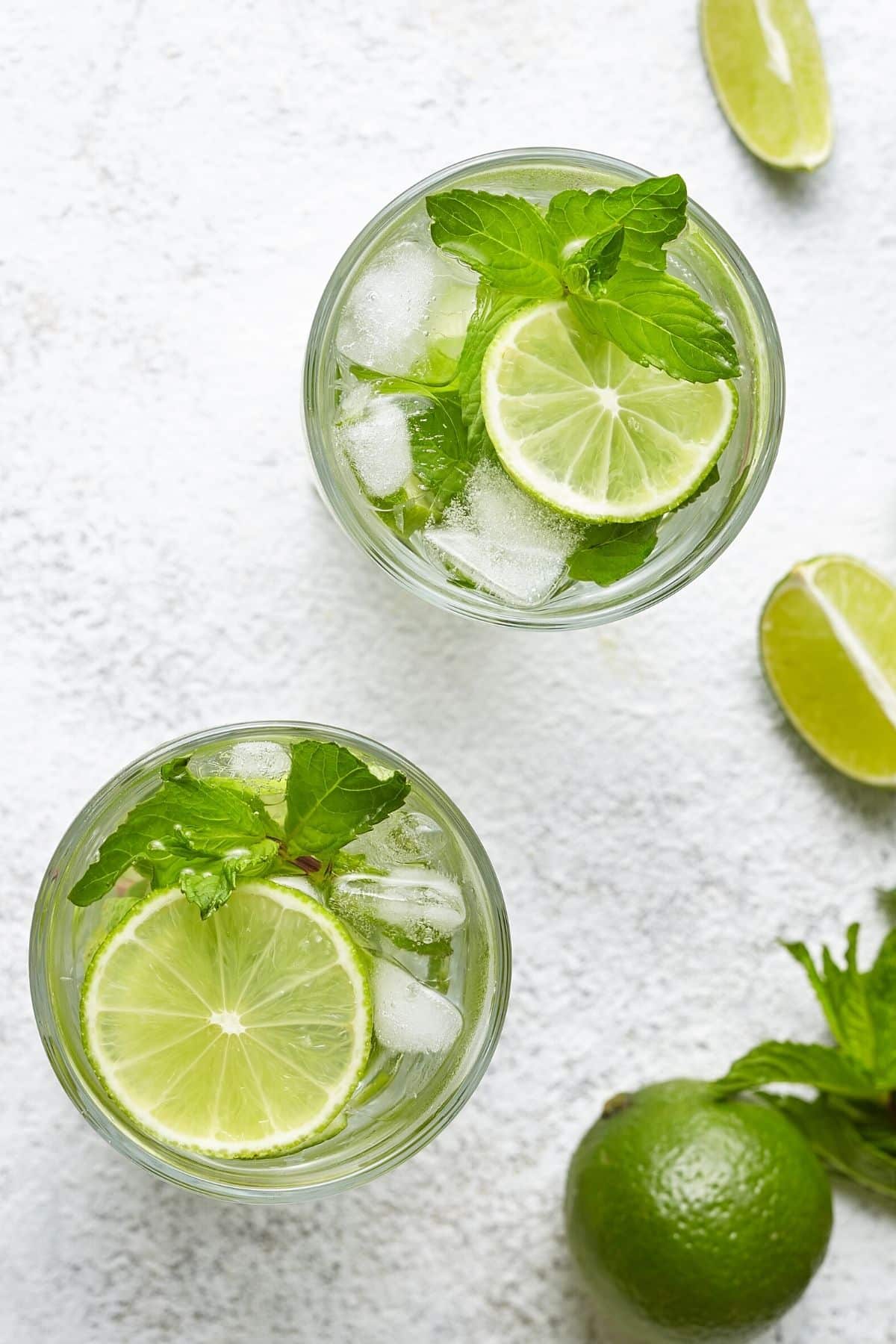 Two clear glasses filled with mojito mocktail with limes, mint and ice.
