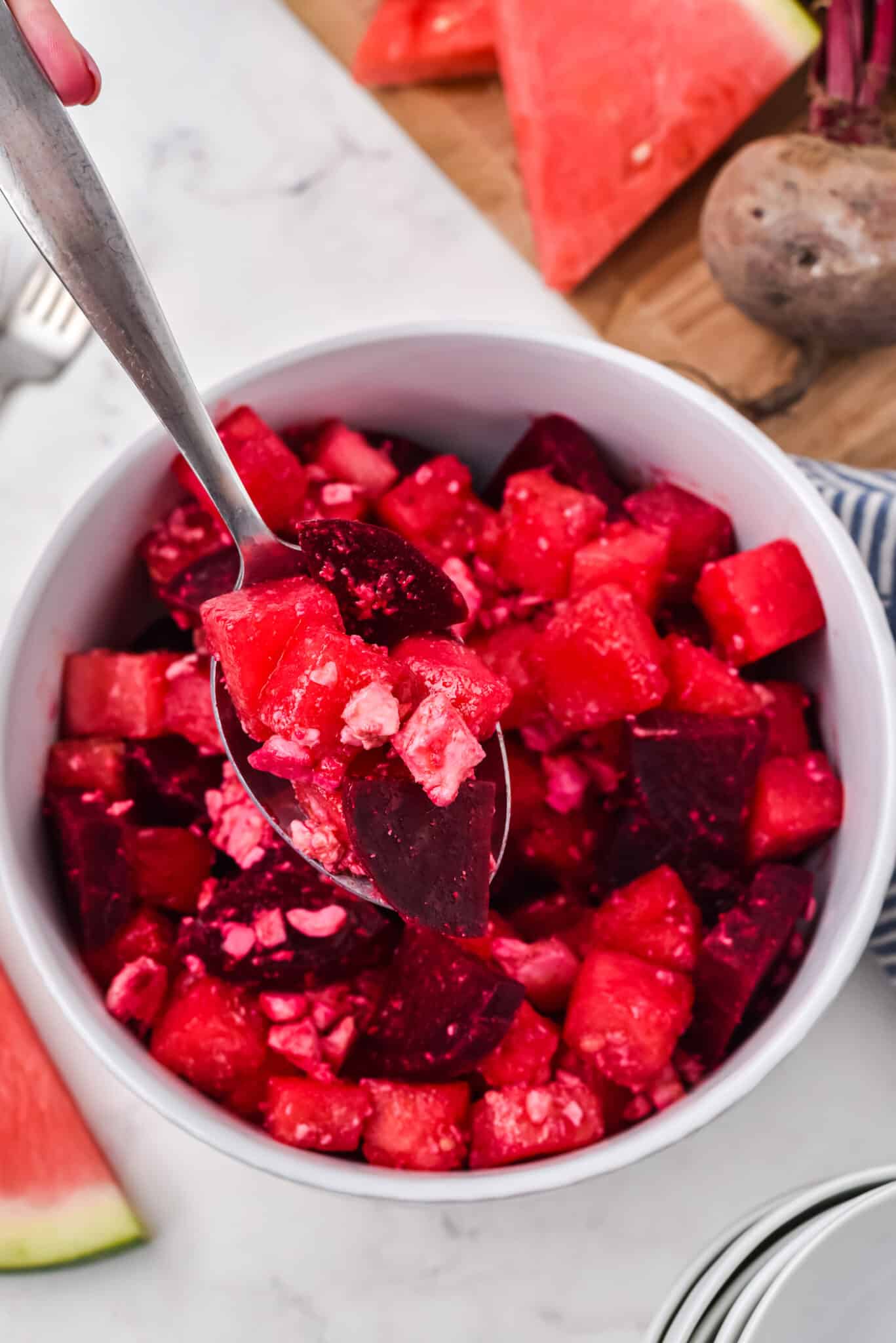 A spoon holding a bit of watermelon beet salad over a small white bowl.