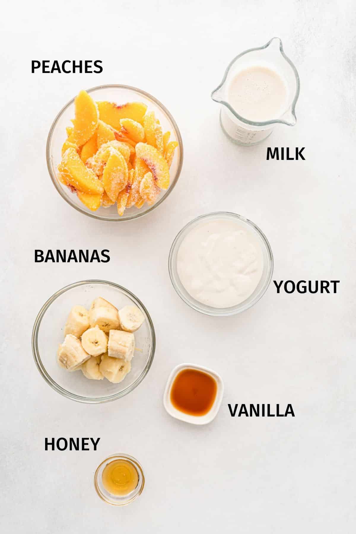 Ingredients for a banana peach smoothie in small bowls on a white surface.