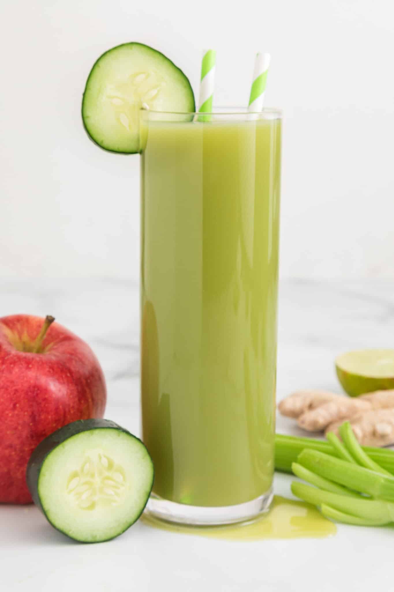 A tall glass of cucumber celery juice with cucumber wheels and straws.