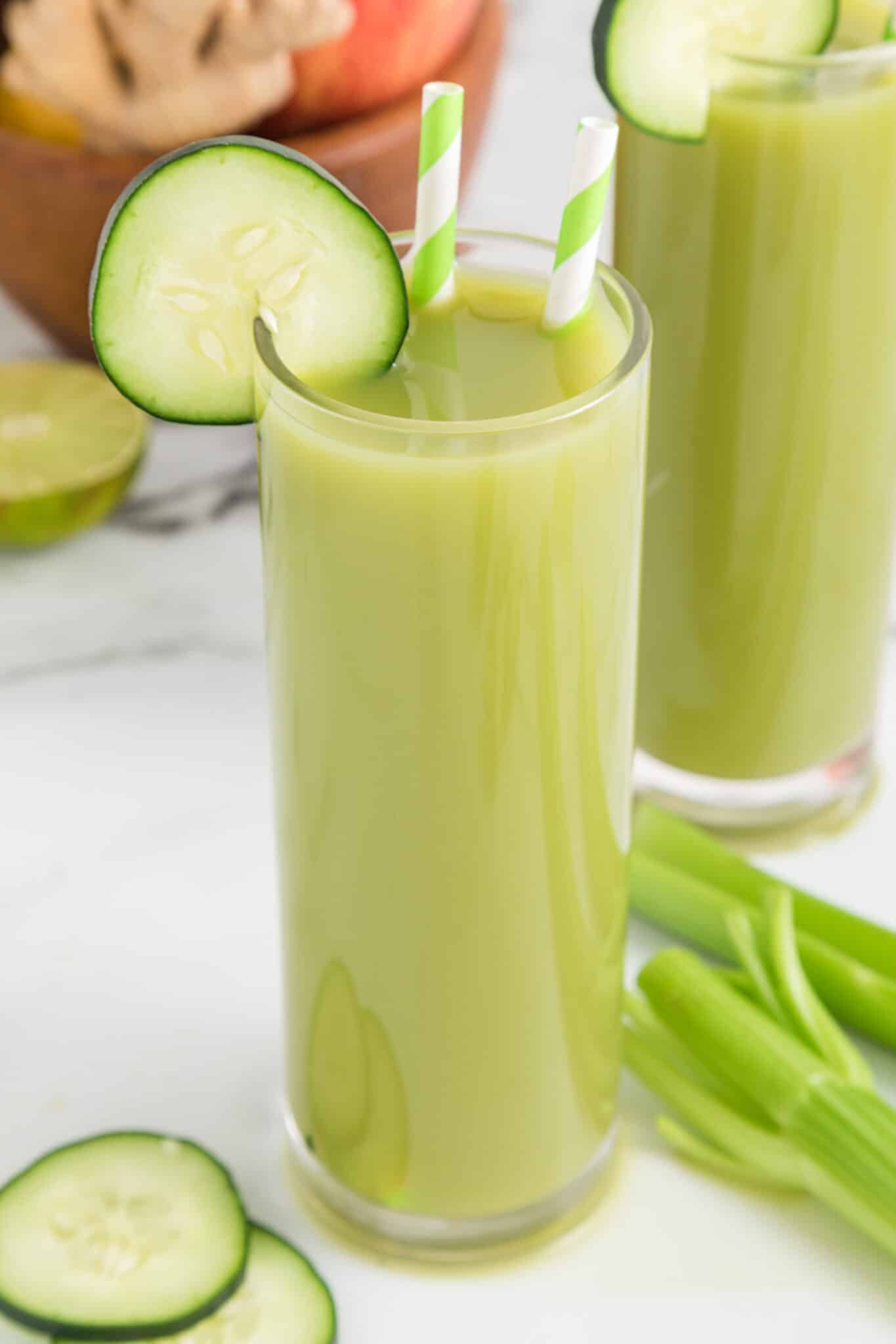 Two glasses of cucumber celery juice with cucumber wheels and straws.