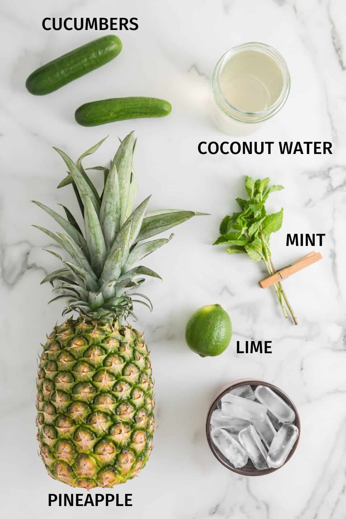 Ingredients to make pineapple cucumber smoothie on a white surface.