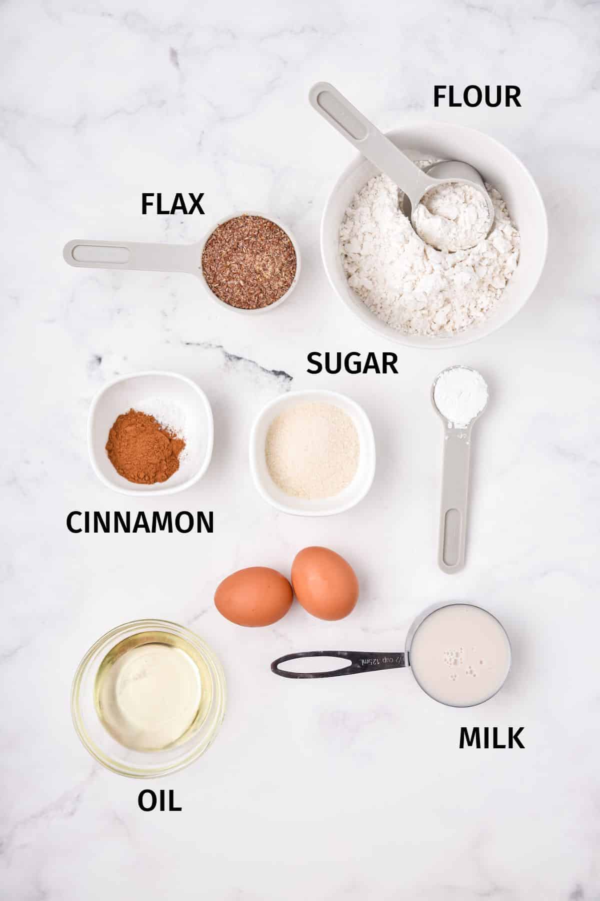 Ingredients to make flax muffins in small bowls on a white surface.
