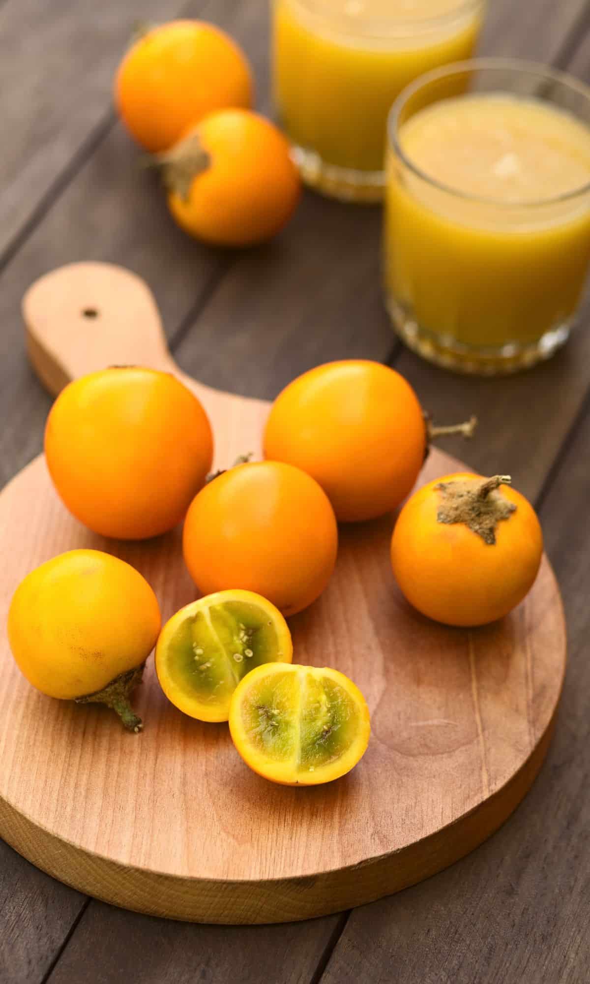 Sliced and whole Naranjilla fruits on a wood slice.