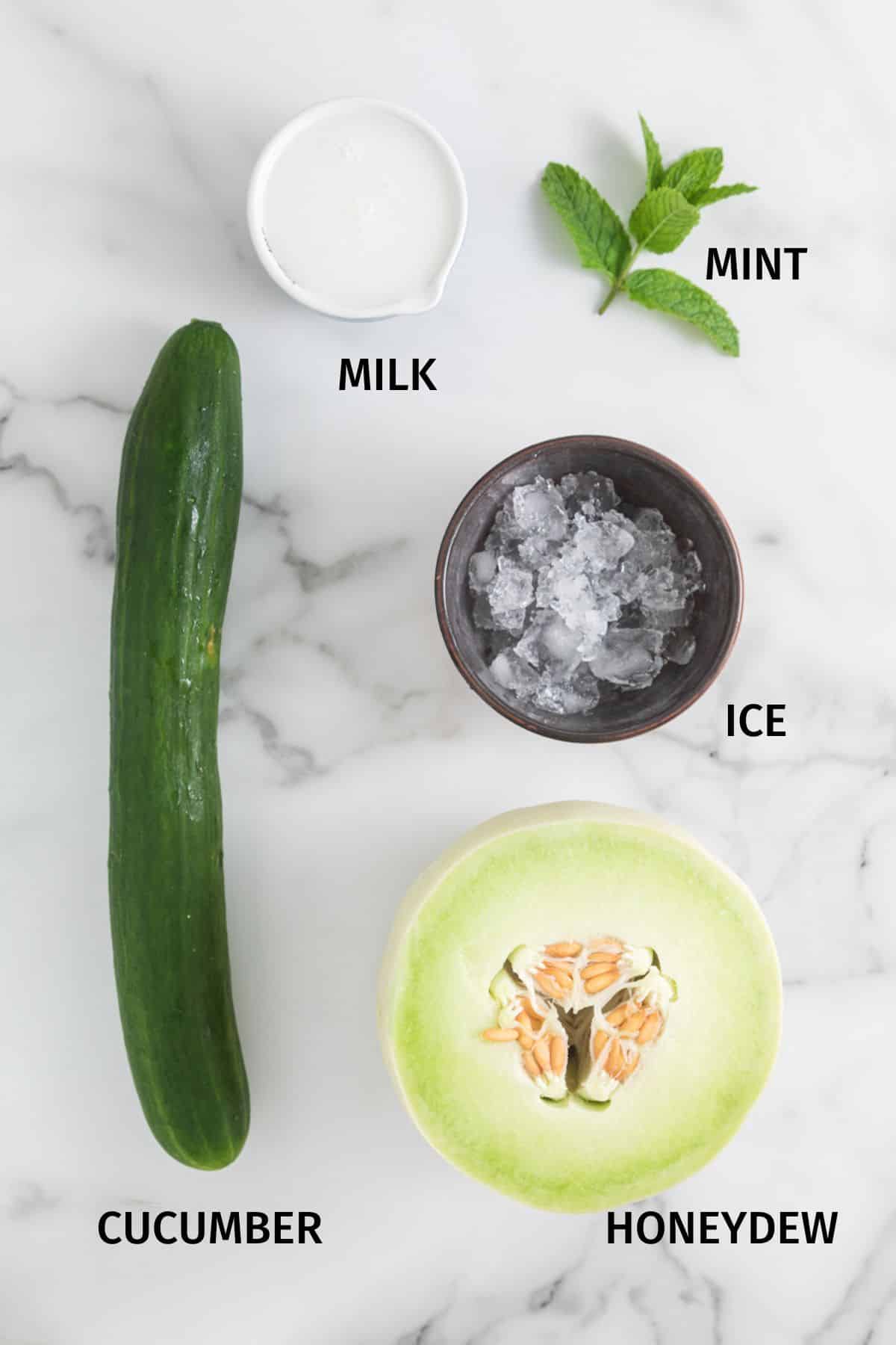 Ingredients to make Honeydew Cucumber Smoothie laid out on a white surface.