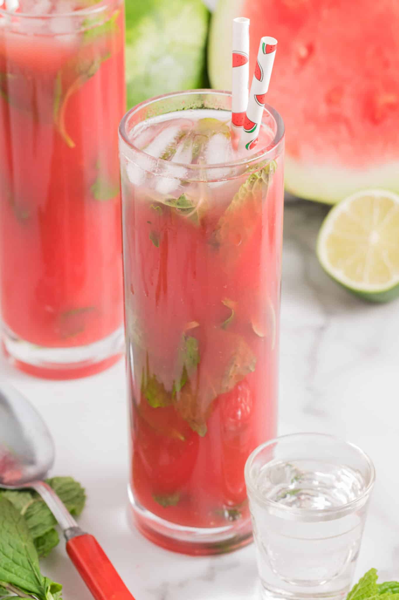 A tall glass filled with watermelon vodka cocktail and a straw.