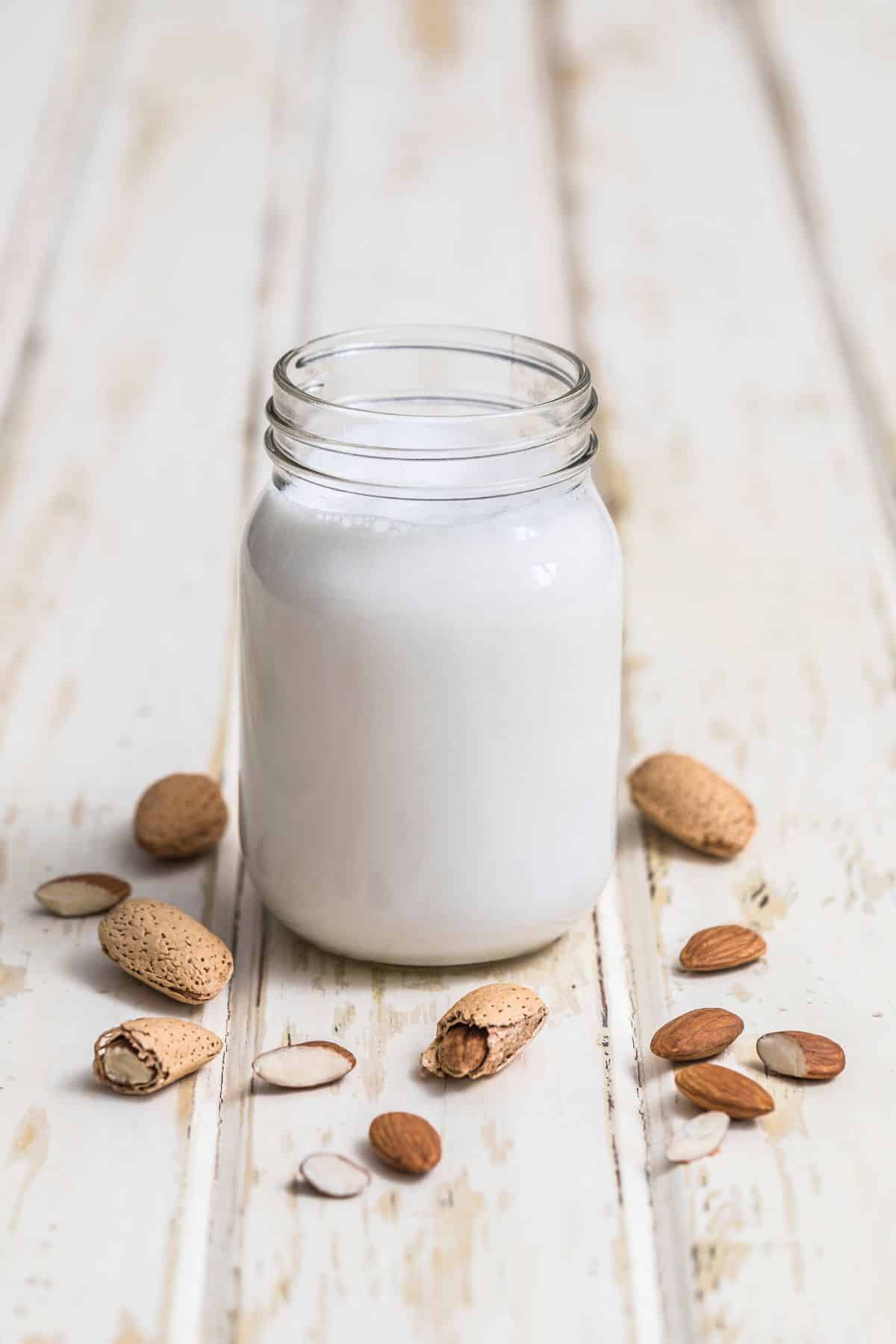 Glass of almond milk with almonds on white table.