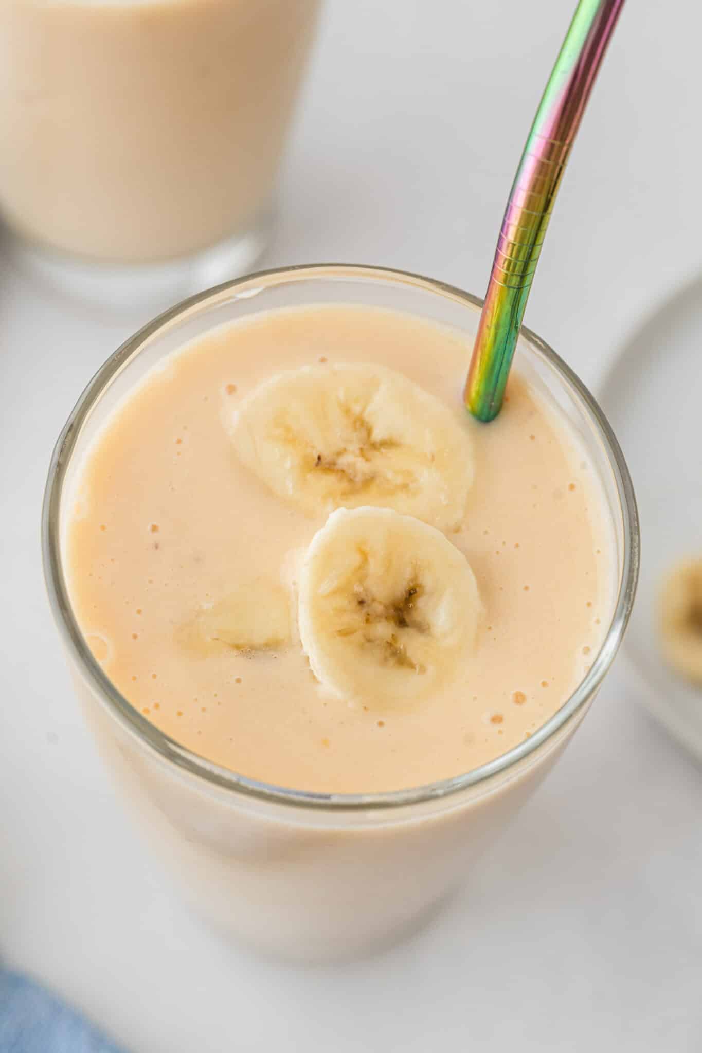 Close up of banana slices on top of a glass of banana peach smoothie.